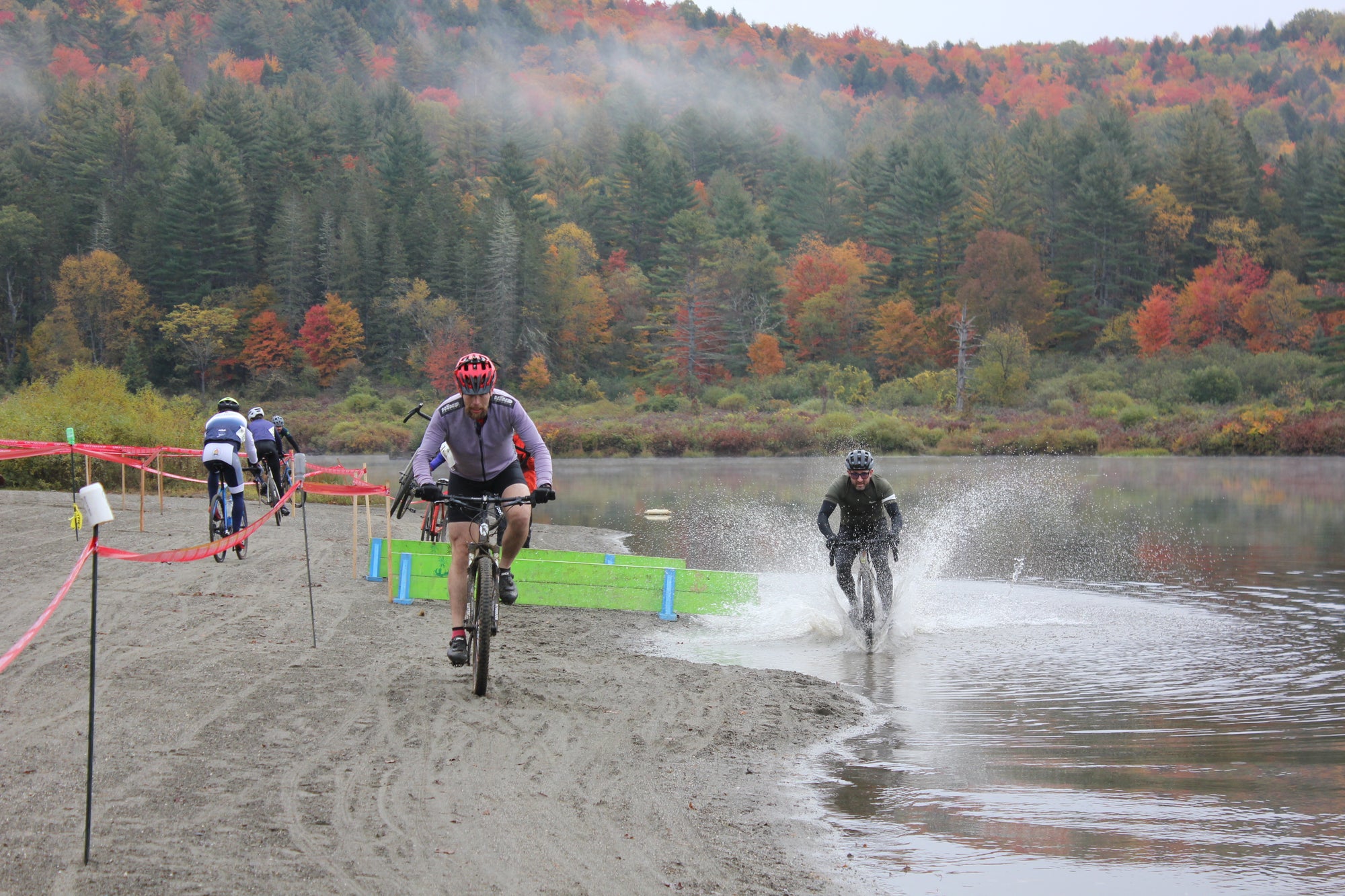 Two bike riders racing cyclocross through sand and water