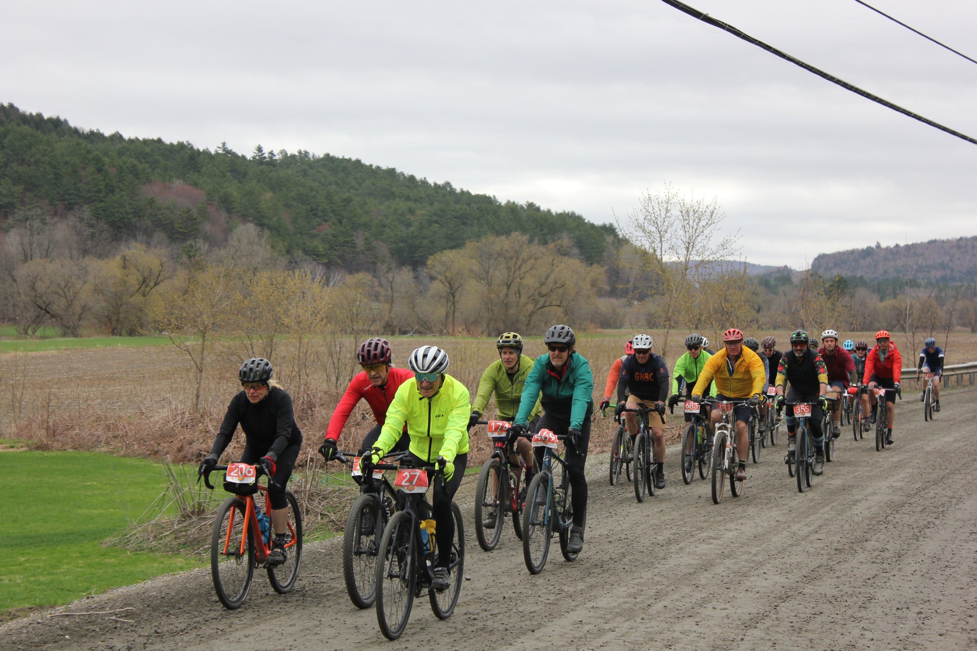 A large group of cyclists in bright colors riding a gravel road