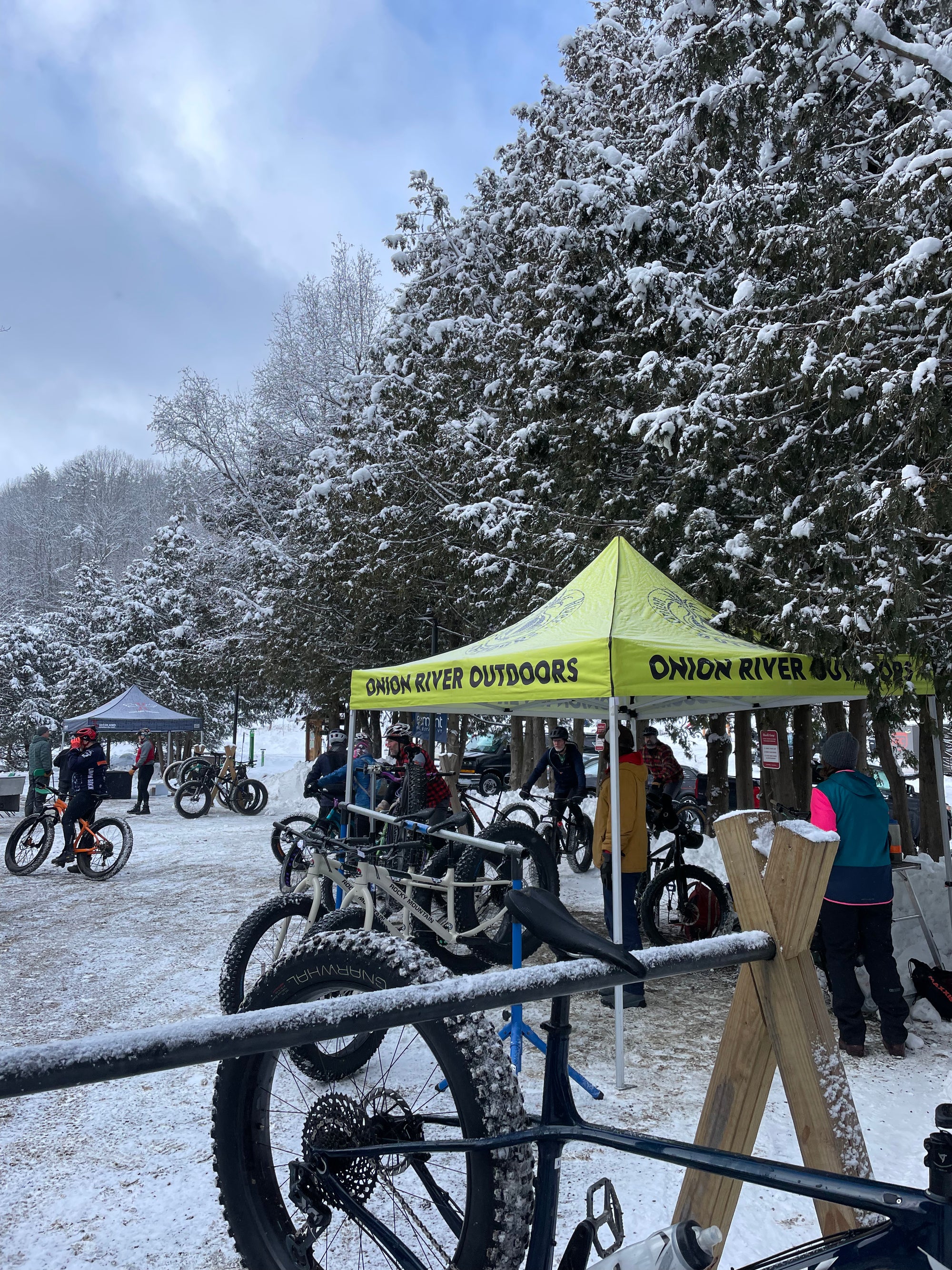 A fat bike hanging from a rack with a bright yellow event tent behind on a snowy day