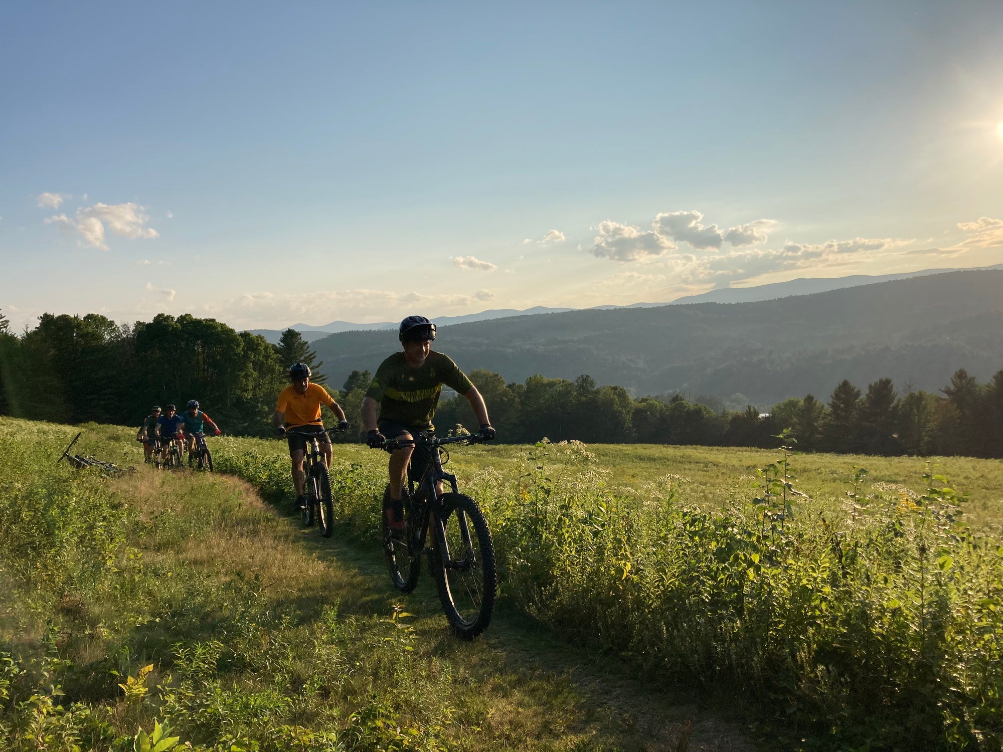 A mountain biker waving riding in a field with a couple riders behind them