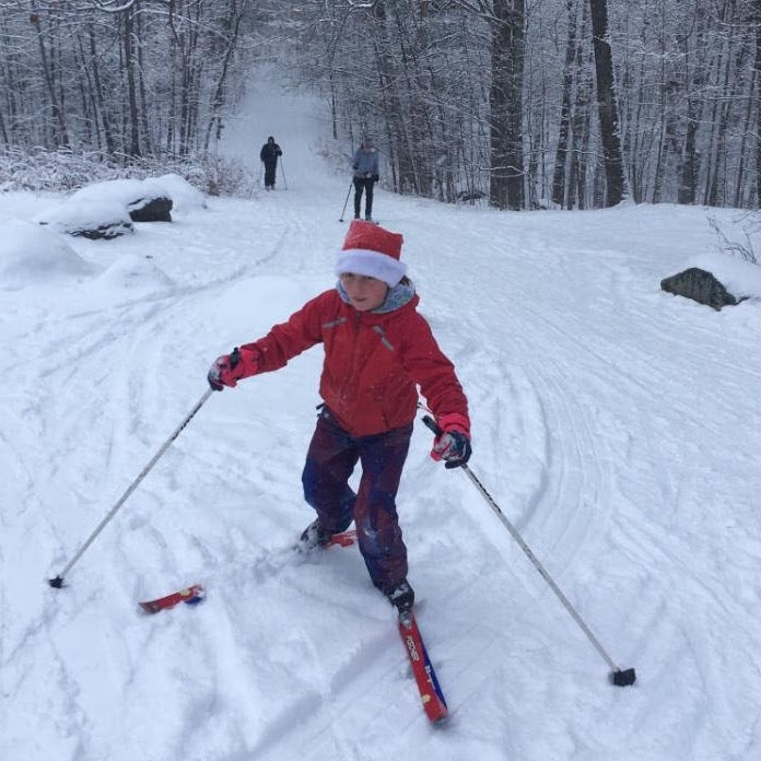 A kid skiing uphill on cross country skis with two skiers in the distance 